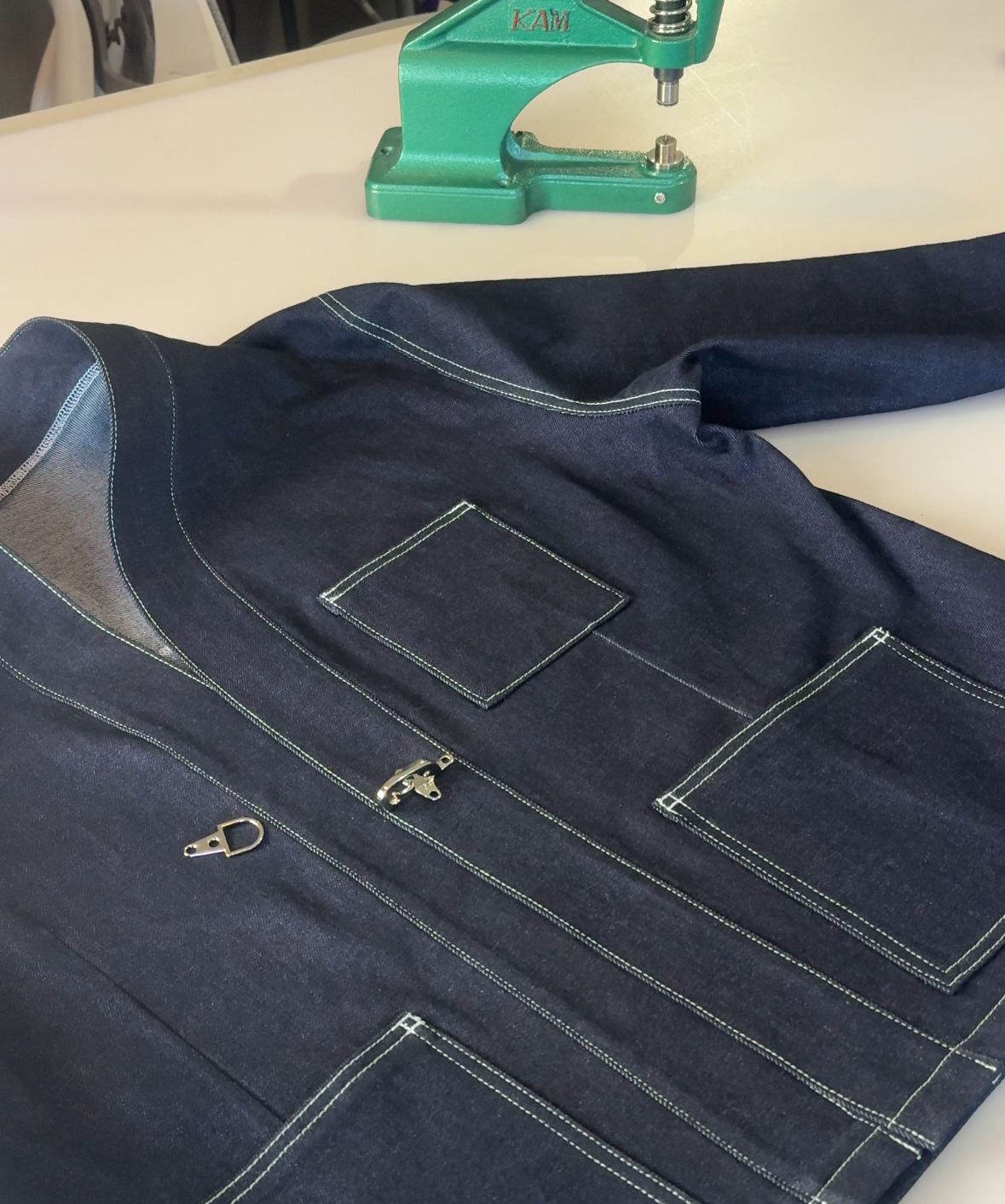 Navy blue jacket on a white surface with a green tool in the background