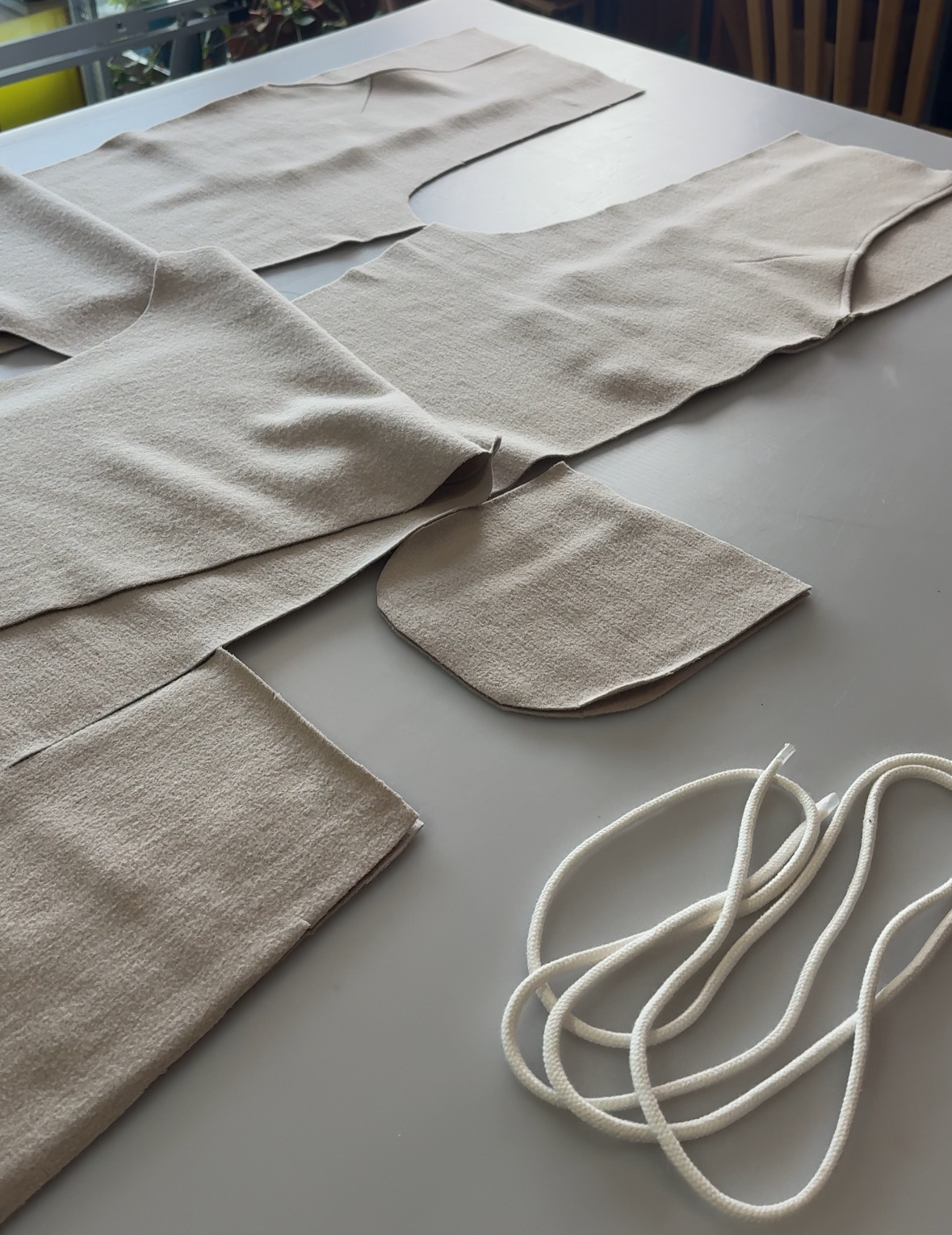 Beige fabric pieces and a white cord on a light-colored surface with a blurred background.
