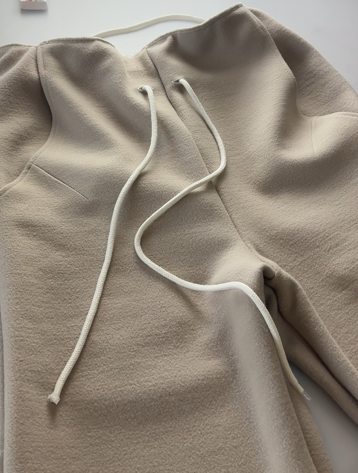Beige hoodie with white drawstring on a light gray surface